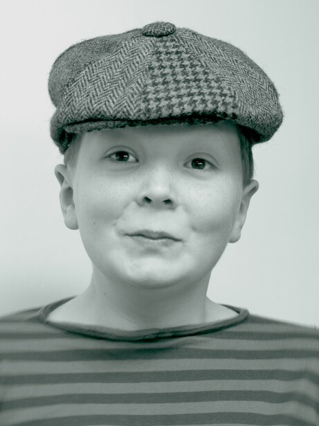 Black and white portrait of a person wearing a flat cap and striped shirt against a neutral background.