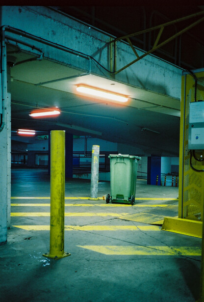 Underground parking garage with yellow support columns, fluorescent overhead lighting, and geometric floor markings.