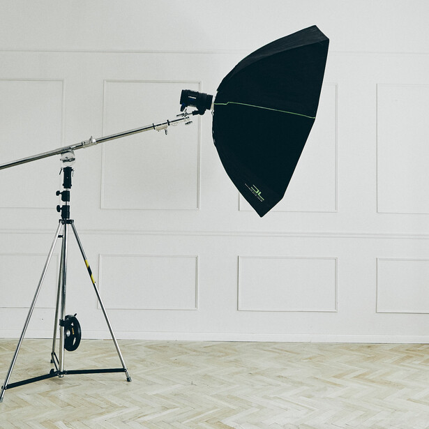 Professional studio lighting setup with large black parabolic reflector mounted on boom arm and tripod stand.