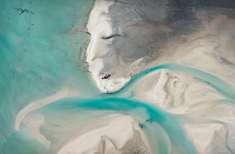 Aerial view of turquoise waterways winding through white sand banks and shallow coastal waters.