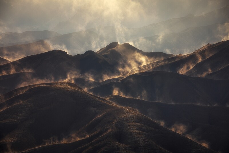 Mountainous landscape engulfed in wildfire smoke and flames during golden hour.