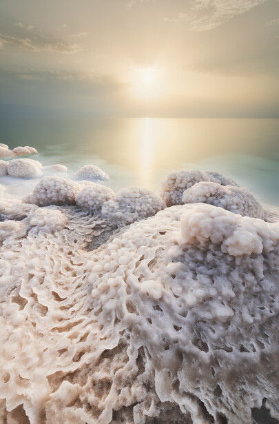 Frost-covered rocks in the foreground with a frozen lake and golden sunrise reflecting on water in the background.