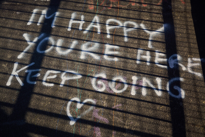 Shadow cast by a railing across weathered wooden steps with chalk graffiti text.