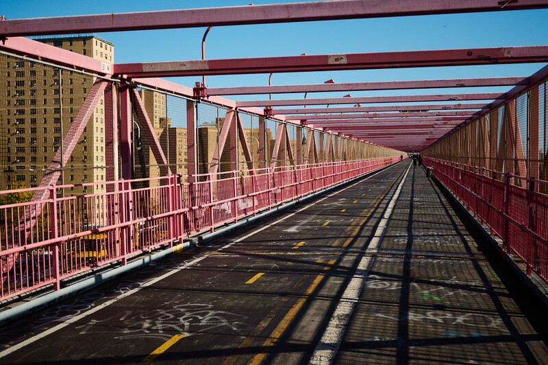 Red steel pedestrian bridge stretching into distance with strong linear perspective and geometric shadows.