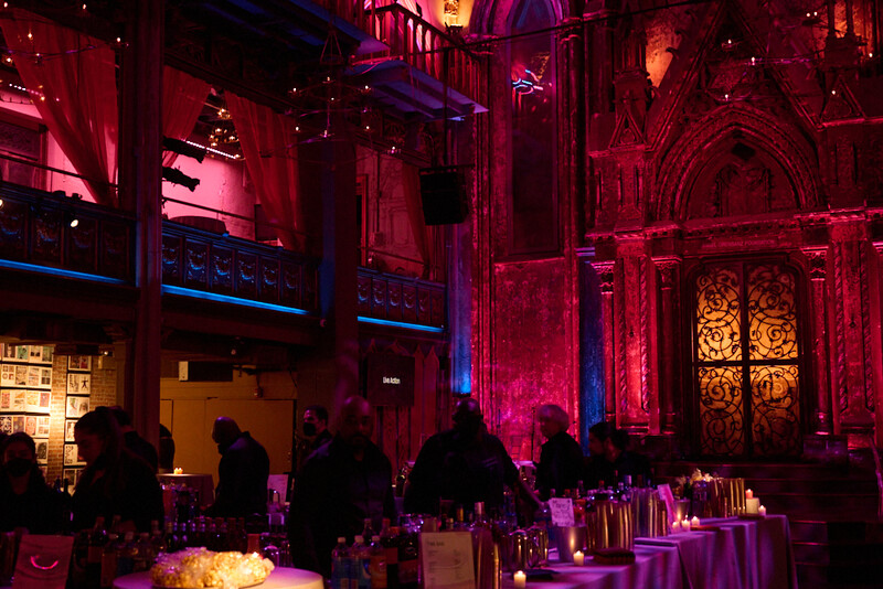 Interior of a grand Gothic-style building lit with dramatic red and purple uplighting, with silhouetted guests and elegant table settings below.