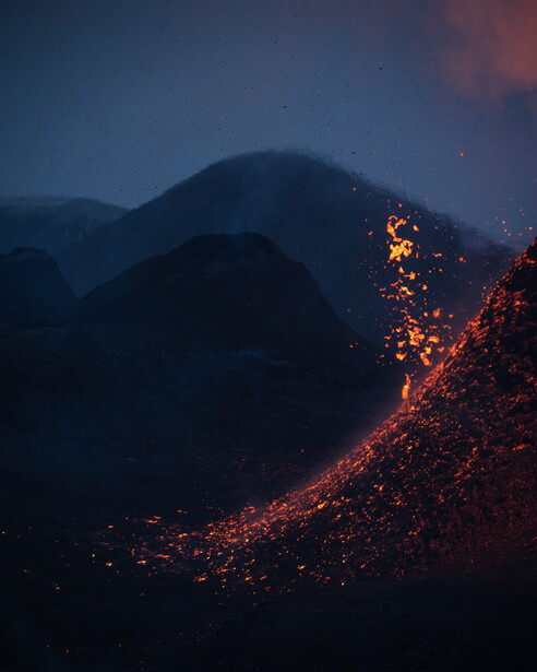 Lava flowing down a volcanic mountainside at night, glowing orange and red against dark slopes.