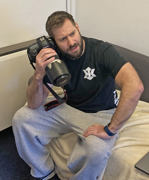 Photographer holding a telephoto lens while sitting indoors, demonstrating equipment handling.
