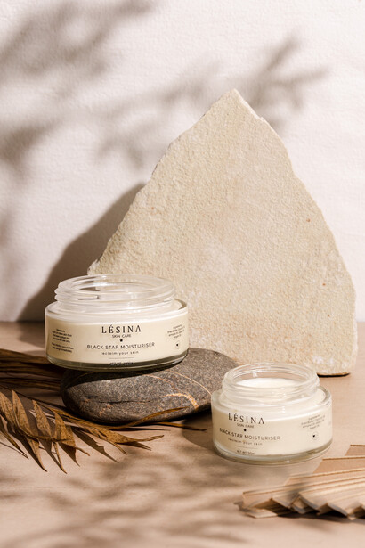 Minimalist product photography setup with cream-colored jars, natural stone, dried botanicals, and geometric backdrop with window shadows.