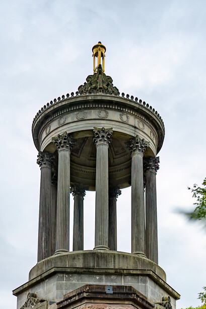 Classical cylindrical monument with tall Corinthian columns and domed top featuring a golden finial.