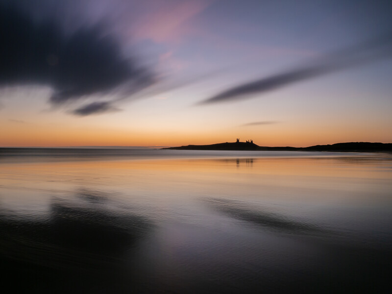 Calm seascape at dusk with silhouetted islands and long-exposure blurred water.