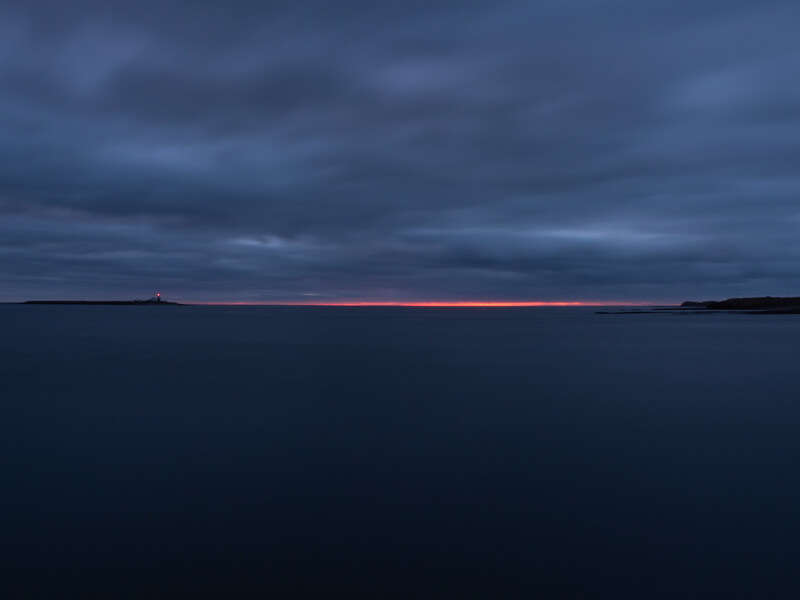Twilight seascape with dark storm clouds above calm water and a thin pink horizon line.
