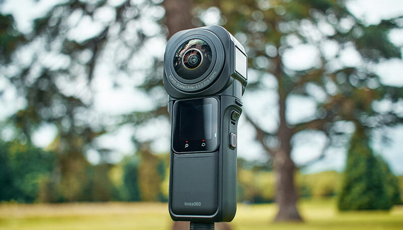 Compact spherical action camera mounted on a stand against an outdoor park backdrop with blurred trees.