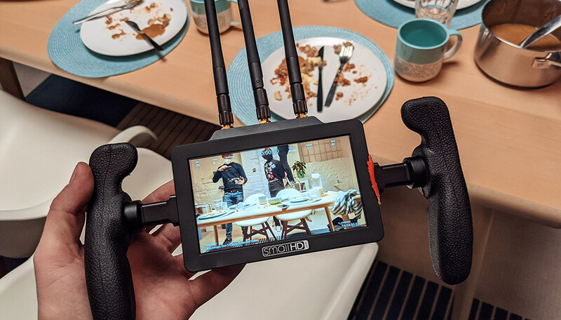 Hands holding a portable monitor displaying video footage of an interior space during a meal.