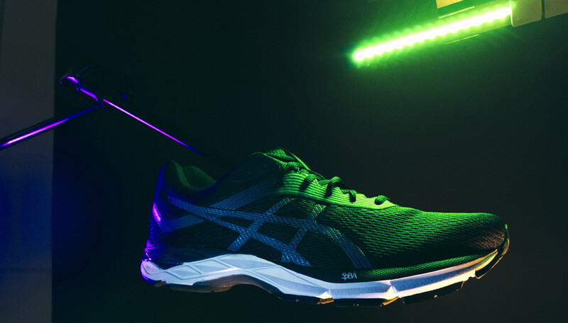 Running shoe suspended against dark background with neon green and purple lighting creating dramatic shadows.