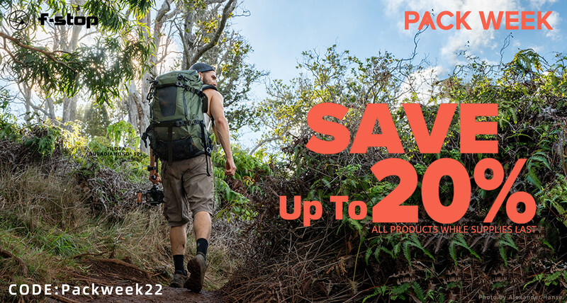 Hiker with backpack walking on overgrown trail through dense vegetation under bright sky.