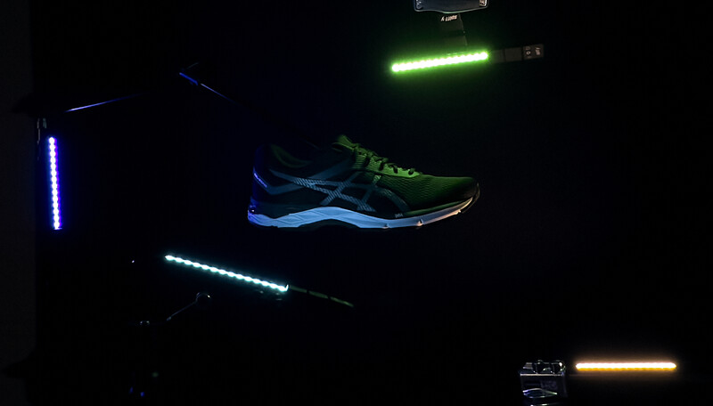Running shoe with neon green and blue accents displayed against dark background with colorful LED light strips.