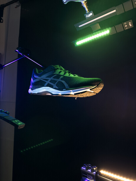 Athletic shoe suspended in mid-air against dark background with neon green and blue accent lighting.