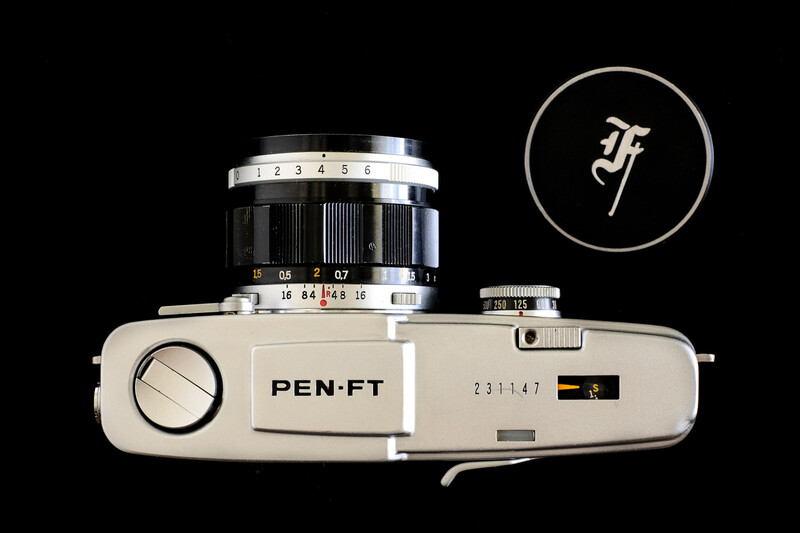 Top-down view of a vintage Pen-FT film camera with chrome lens and cream-colored body against black background.