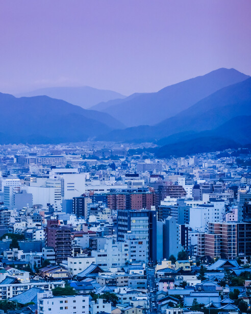 Cityscape with densely packed buildings and mountains under blue hour lighting.