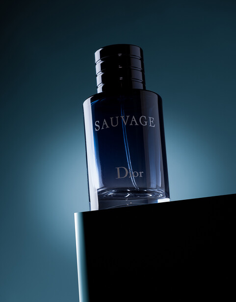 Dior Sauvage fragrance bottle positioned on a black platform against a teal gradient background.