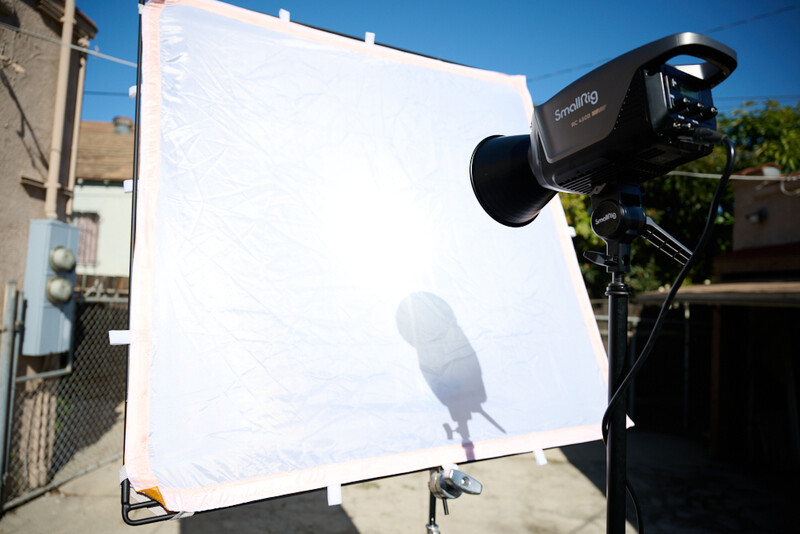 Film camera mounted on a stand pointing at a white reflector panel with a microphone shadow cast on it.