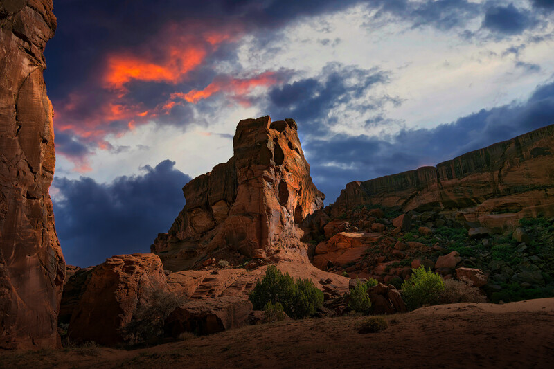 Towering rock formation silhouetted against a dramatic sunset sky with orange and blue clouds.