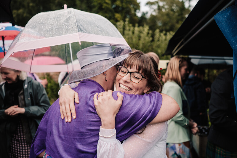 Two people embracing in the rain under umbrellas at an outdoor event.
