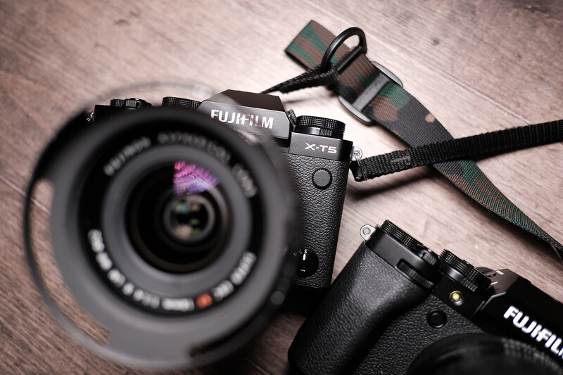 Fujifilm camera with attached lens and camera strap on wooden surface.