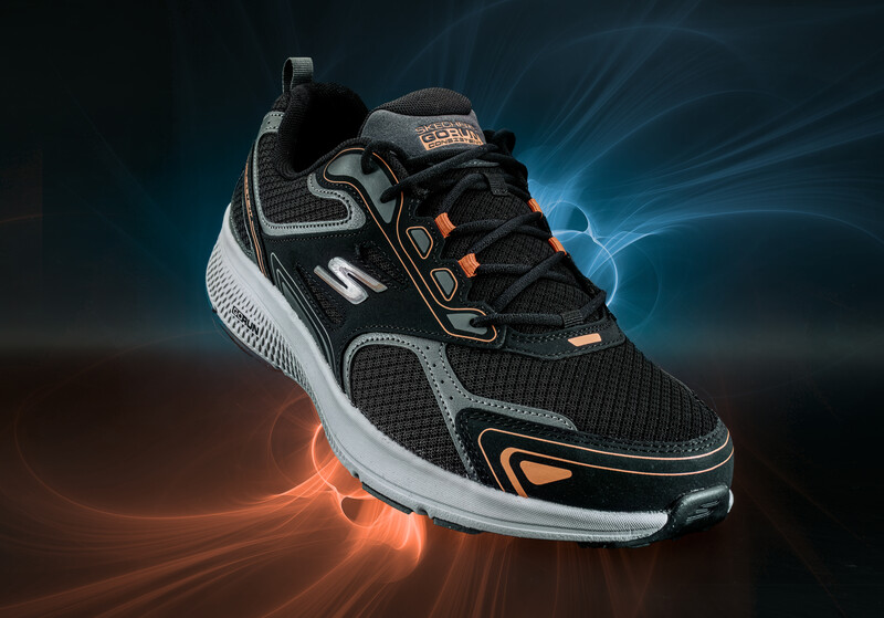 Black and white athletic shoe with orange accents photographed against dramatic blue and orange light trails.
