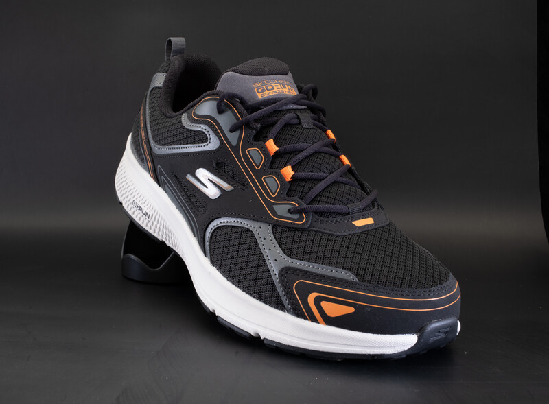 Black, white, and orange athletic sneaker photographed against a dark gray background.