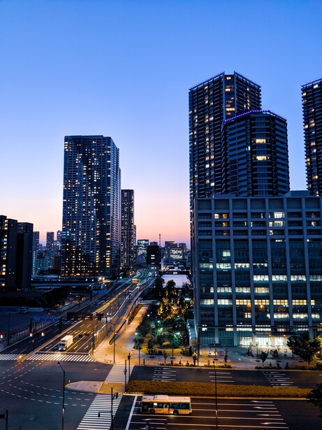 Illuminated skyscrapers at dusk with light trails from traffic below in an urban downtown area.
