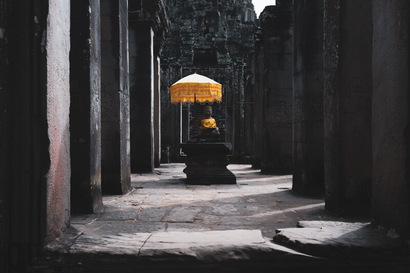 Person with yellow umbrella standing in a narrow stone corridor with dramatic side lighting.