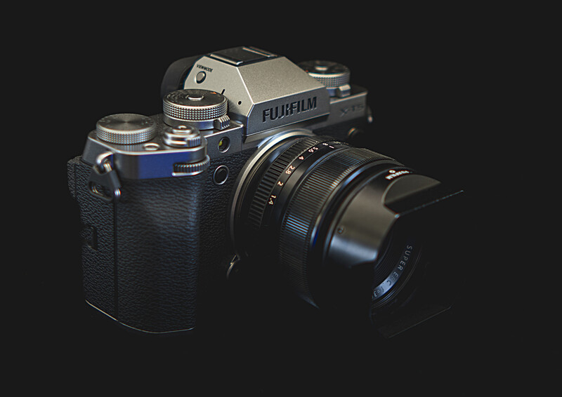 Fujifilm mirrorless camera with attached lens on dark textured surface.