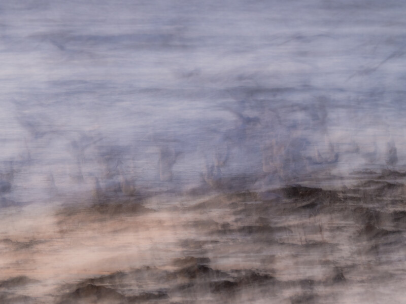 Ocean waves with motion blur washing onto a sandy beach under an overcast sky.