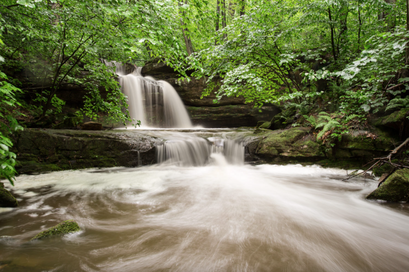 Tiered waterfall flowing through a lush forest with smooth water motion blur.