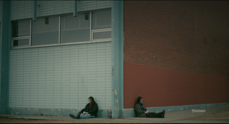 Two people sitting separately against a colorful urban wall with geometric architecture.