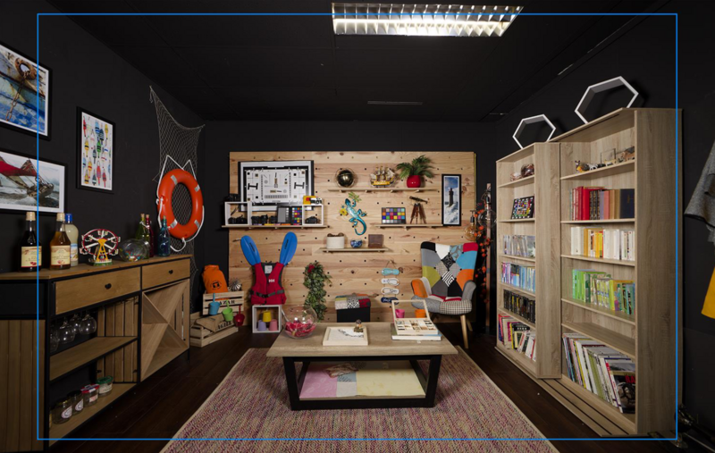 Creative studio workspace with colorful organizational systems, shelving, mood boards, and natural wood furniture against dark walls.