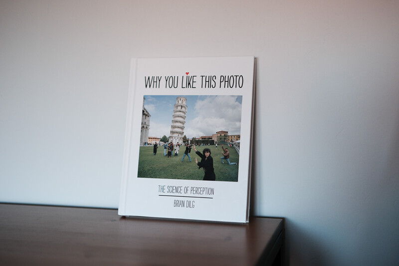 Printed photo book titled 'Why You Like This Photo' displaying a leaning tower and crowd scene.