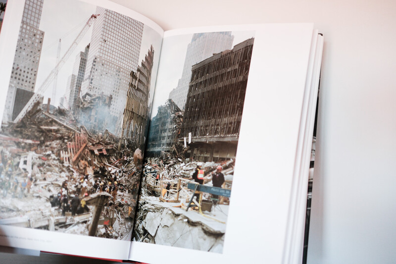 Open photography book displaying a two-page spread of urban destruction and debris with tall buildings surrounding the scene.