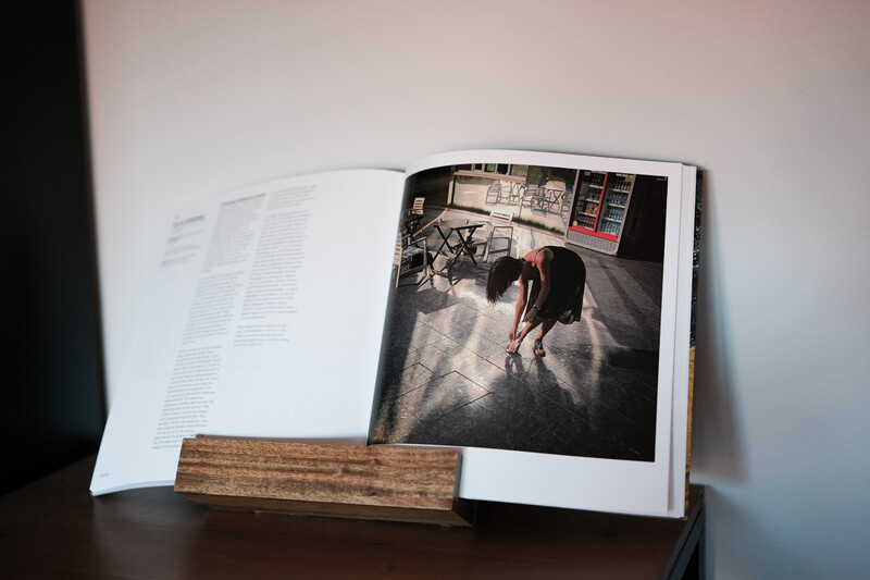 Open photography book displayed on wooden stand showing interior spread with photograph and text.