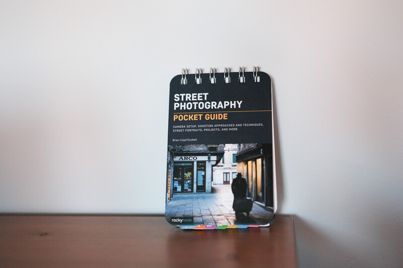 Spiral-bound Street Photography Pocket Guide resting on a wooden surface against a white wall.
