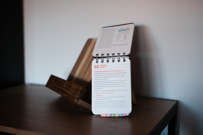 Spiral-bound notepad with colored page tabs displayed on a wooden stand next to rolled documents.