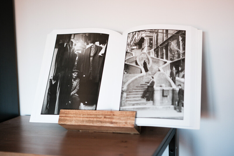 Open photo book with black and white photographs displayed on wooden stand.