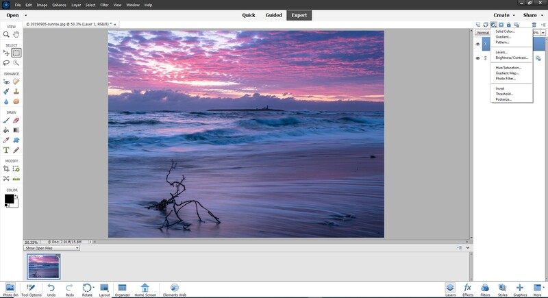 Driftwood silhouette on a beach at sunset with purple and pink sky reflecting in wet sand.