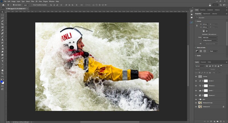 Whitewater kayaker in yellow jacket and white helmet paddling through turbulent rapids.