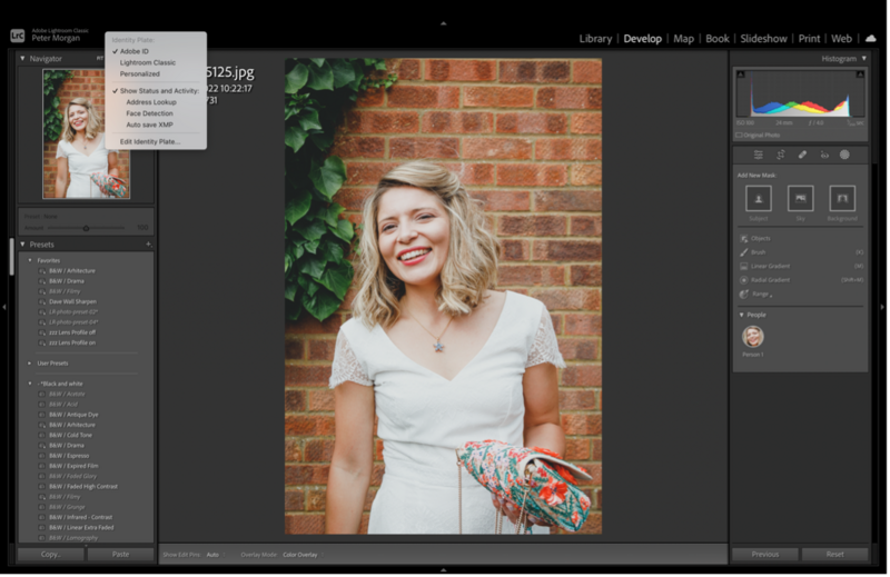 Woman in white v-neck shirt smiling at camera against brick wall with ivy.