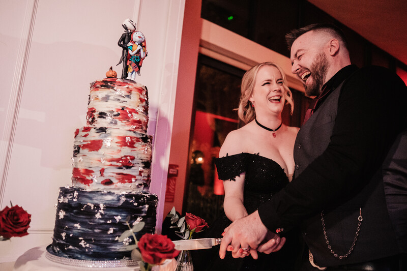 Couple cutting a tiered wedding cake with red floral decorations and a cake topper.