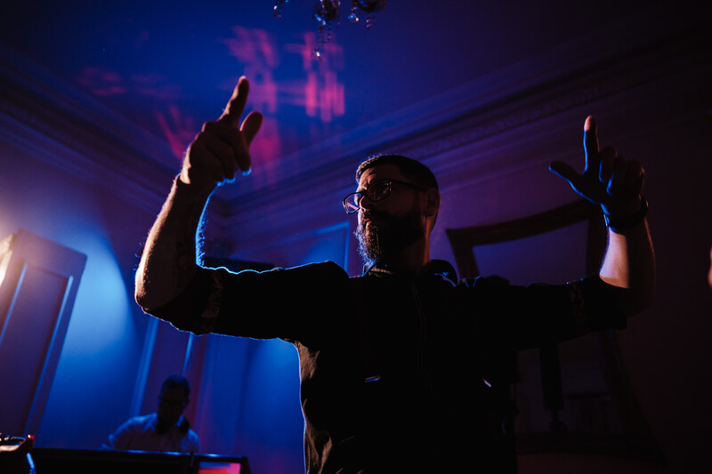 Silhouetted performer on stage with arms raised, bathed in blue and purple stage lighting.