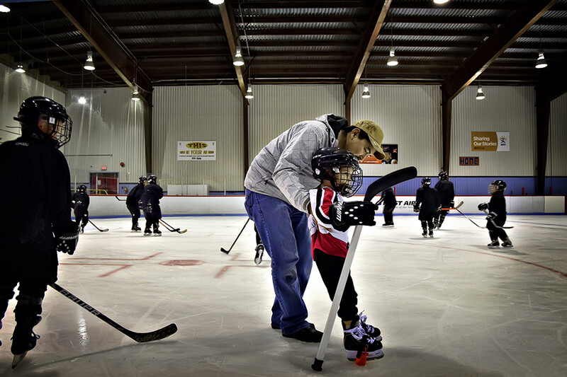 Adult instructing young hockey player during ice rink practice session.