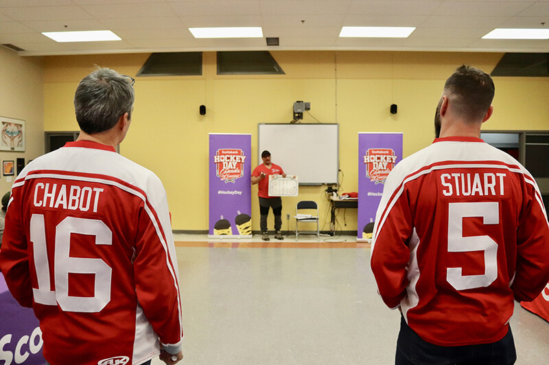 Two people wearing red and white sports jerseys with numbers 16 and 5 facing away toward a gymnasium with yellow walls.